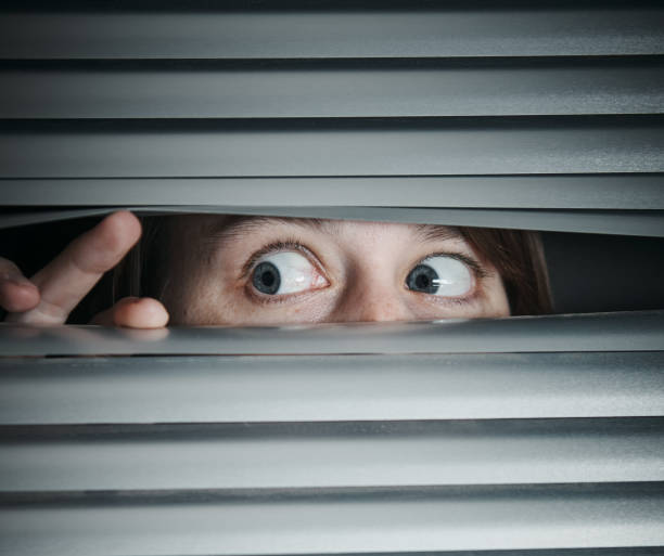istock Terrified young woman peeps sideways through blinds 1168128132