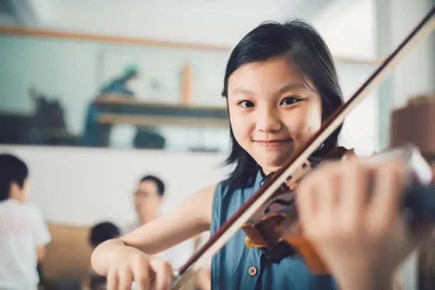 Photo of Asian Little Girl playing violin at home.