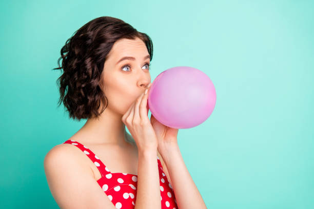 photo of pretty lady with air ballon in mouth wear red dotted dress isolated teal background - inflating balloon blowing air imagens e fotografias de stock