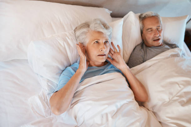 You'd have thought I'd be used to his snoring Cropped shot of a senior woman blocking her ears in frustration while her husband snores in bed beside her sleep apnea photos stock pictures, royalty-free photos & images