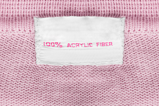 Clothes label says 100% acrylic fiber on pink knitted background closeup