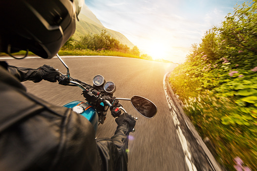 View from motorcycle driver perspective riding in Alpine landscape during sunrise
