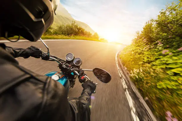 View from motorcycle driver perspective riding in Alpine landscape during sunrise