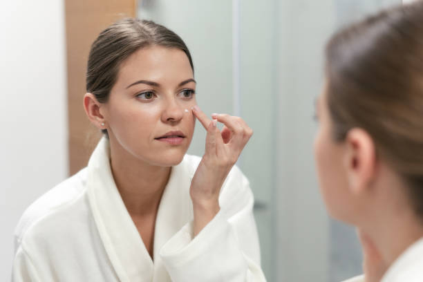 istock Woman standing in bathroom, applying cream on face 1168144592