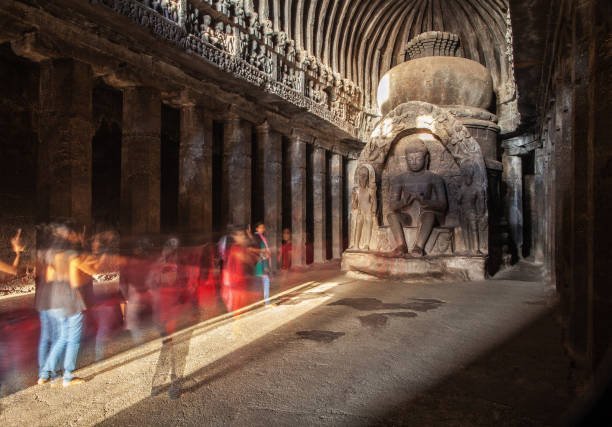 Buddha carved in stone - as an image of constancy of the teaching. Shot with long exposure - blurred groups of tourists, as if an image of a temporary essence of all live. Buddha carved in stone, sitting on a throne in beams setting the sun - as an image of constancy of the teaching. ajanta caves photos stock pictures, royalty-free photos & images