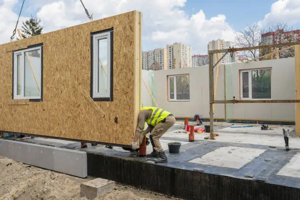 Process of construction new and modern modular house from composite sip panels. Worker man in special protective uniform wear working on building development industry of energy efficient property