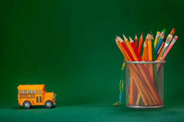 Education and back to school concept. Yellow retro school bus and pencils in basket on dark green background.