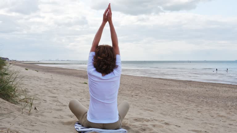 Mature woman meditating in Lotus Pose on the beach