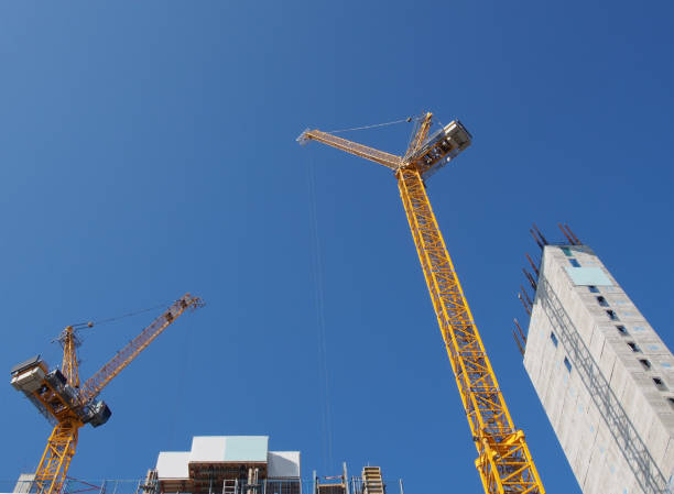 istock two tall yellow tower cranes working on a large residential construction site with a large concrete tower against a blue sky 1168168136