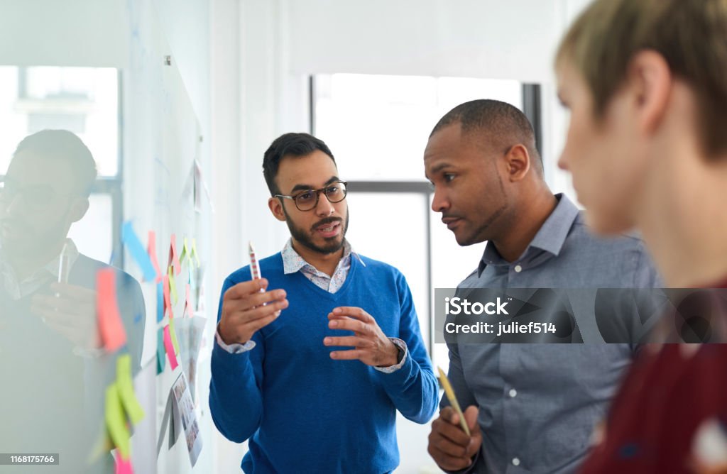 Portrait of an indian man in a diverse team of creative millennial coworkers in a startup brainstorming strategies Multi-ethnic group hipster trendy business people with Indian boss discussing during a brainstorm session for their small company Business Stock Photo