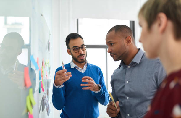 Portrait of an indian man in a diverse team of creative millennial coworkers in a startup brainstorming strategies Multi-ethnic group hipster trendy business people with Indian boss discussing during a brainstorm session for their small company topics stock pictures, royalty-free photos & images