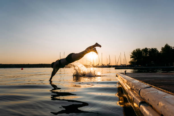 istock Summer day: young woman jump from jetty into lake while sunset 1168180509