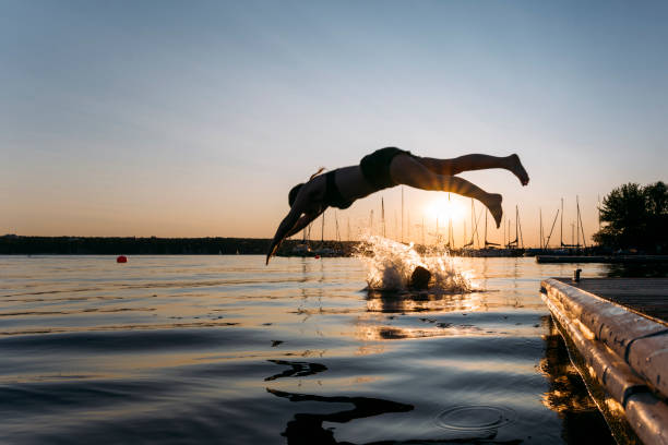 istock Summer day: young woman jump from jetty into lake while sunset 1168180536