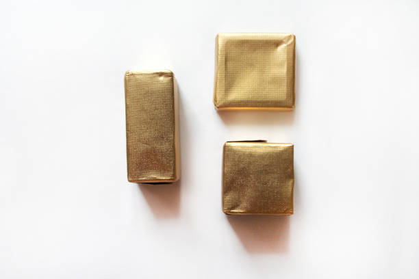Chocolate candies wrapped in golden foil isolated on white surface. Template for greeting card, poster or invitation. Sweets scattered on white smooth table. Backdrop or background. Top view
