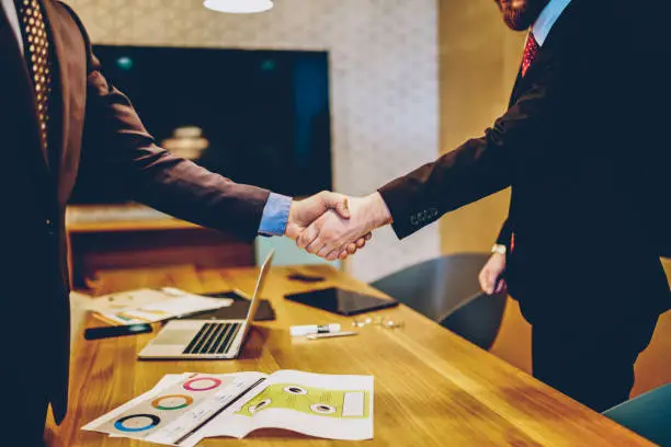 Photo of Cropped image of men in suits shaking hands making deal of sponsorship in business corporation, male entrepreneurs agree in partnership cooperation and contract during formal meeting in office