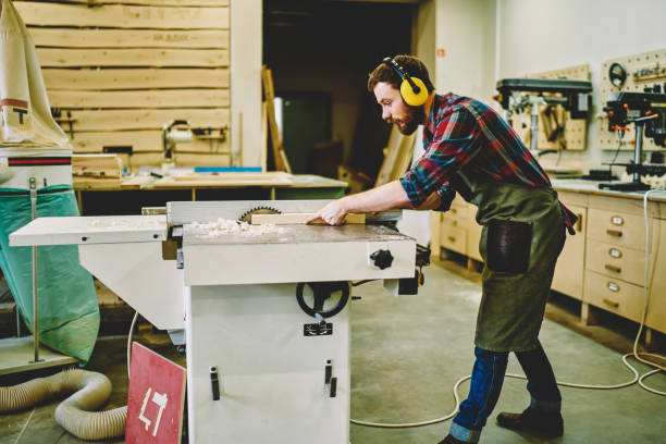 istock Young craftsman concentrated on carpentry work with wooden using circular for saw plank, skilled male joiner in wear for safety and protection during using professional equipment in workshop 1168188488