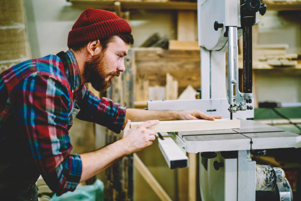 istock Serious bearded guy using modern equipment for making wooden planks in own crafts workshop, skilled male carpentry concentrated on work with timber on electric machinery in professional manufacture 1168188550