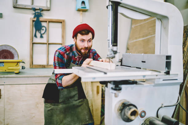 istock Smiling hipster guy satisfied with carpentry courses and learning how to use electric machinery for woodworks, positive caucasian male joiner excited with great job making planks for furniture 1168188566