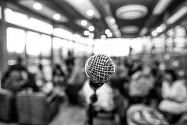 Black and white photo of a microphone infront of defocused people indoors