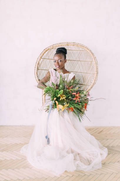 美しい暗い肌の花嫁。スタジオでトロピカルブーケを持つ美しいアフリカ系アメリカ人の花嫁、椅子に座って - wedding african descent american culture bride ストックフォトと画像