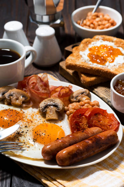 istock Fried eggs with bacon, sausages and vegetables, vertical closeup 1168191080