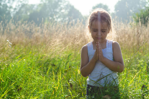 Little girl closed her eyes, praying outdoors, Hands folded in prayer concept for faith, spirituality and religion. Peace, hope, dreams concept. Little girl closed her eyes, praying outdoors, Hands folded in prayer concept for faith, spirituality and religion. Peace, hope, dreams concept. religion sunbeam one person children only stock pictures, royalty-free photos & images