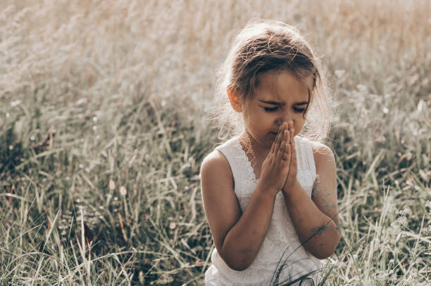 Little girl closed her eyes, praying outdoors, Hands folded in prayer concept for faith, spirituality and religion. Peace, hope, dreams concept. Little girl closed her eyes, praying outdoors, Hands folded in prayer concept for faith, spirituality and religion. Peace, hope, dreams concept. religion sunbeam one person children only stock pictures, royalty-free photos & images