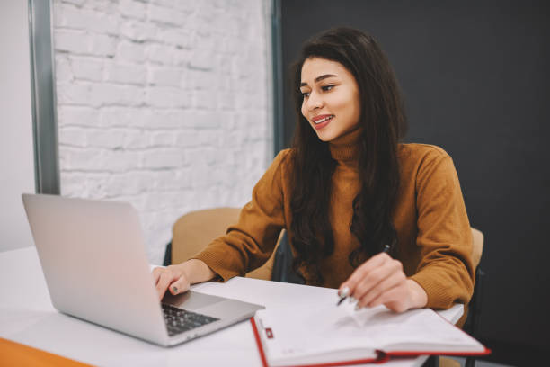 istock Positive female freelancer making online research of information and making notes, smiling young woman studying via online courses by watching learning webinars on laptop computer doing written tasks 1168197011