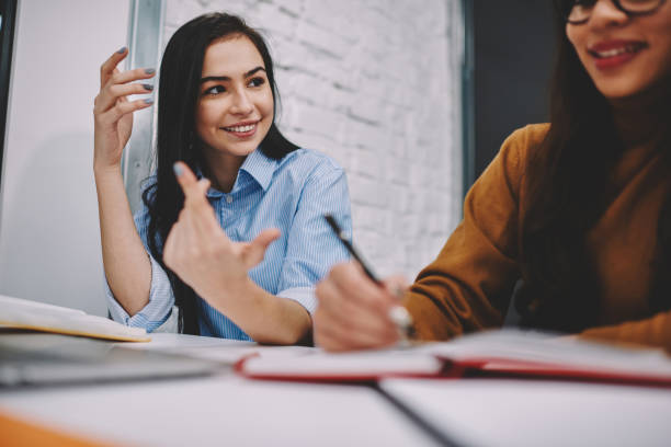 istock Cropped image of smiling female gesturing while explaining something to colleague learning together, happy young women doing homework cooperating and share ideas during working process in campus 1168197023