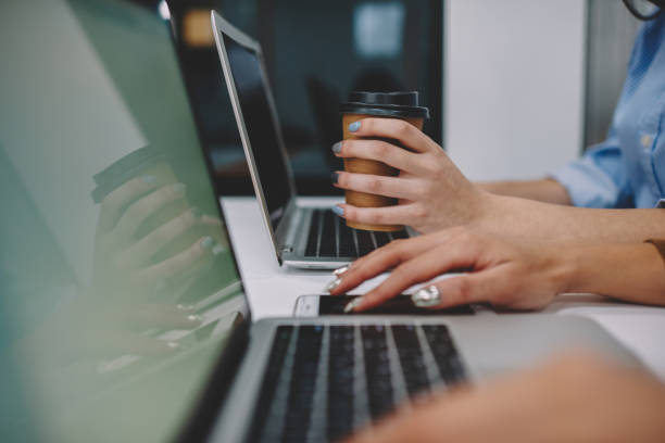 istock Cropped image of woman's hand holding coffee to go cup using caffeine for productive online work via netbook, female connecting smartphone to laptop computer via bluetooth for share multimedia 1168197053