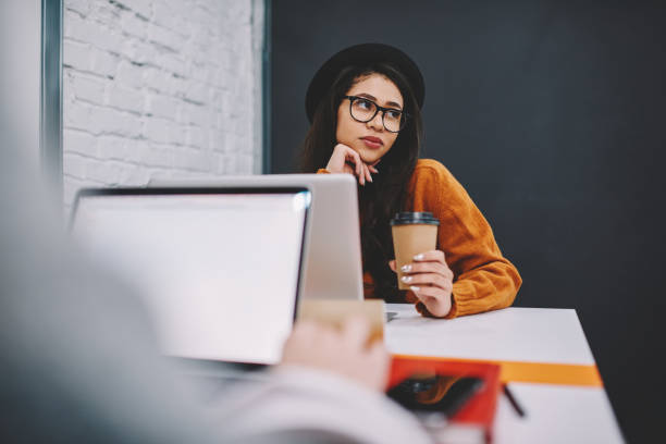 istock Back view image of student working on laptop computer while contemplative friend in cool hat dreamy about successful passed exams, young attractive female person pondering during coffee break 1168197089