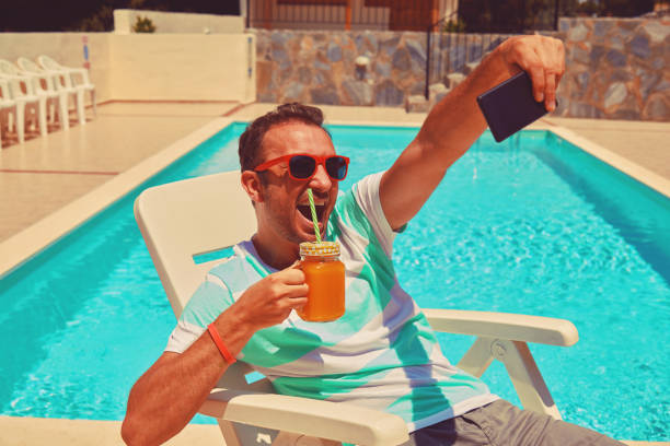 istock Attractive man using cellphone while drinking juice near swimming pool. 1168198508