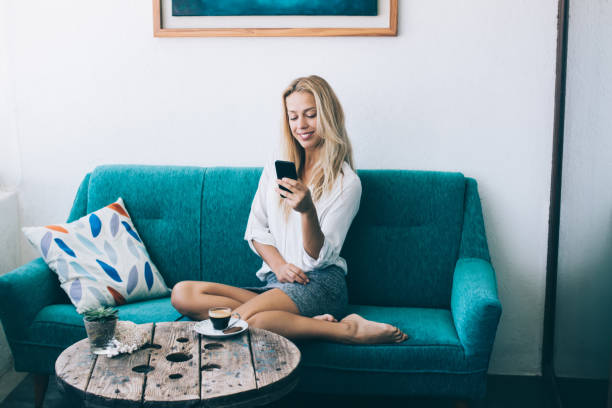 istock Positive woman updating profile in social networks using media application for chatting while sitting on blue comfortable sofa in home interior, happy hipster girl enjoying time with smartphone 1168201483