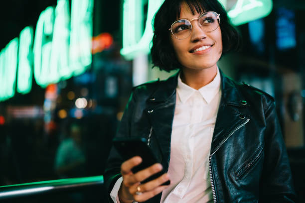 istock Dreamy pretty young woman in eyewear smiling while checking mail on smartphone via 4G internet connection walking in urban setting in eveming time.Puzzled 1168204011
