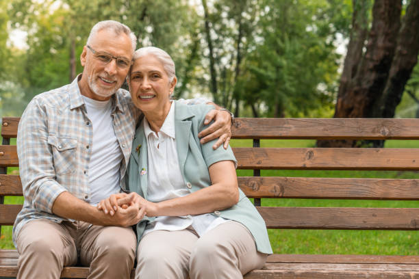 istock Front view of happy senior couple holding hands and looking at camera with smile while sitting on the park bench together 1168206680