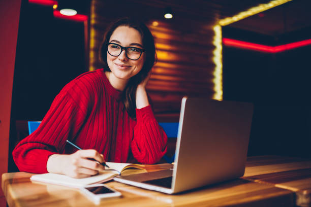 istock Smiling young woman enjoying freelance work in cafe interior making notes of ideas in notepad, positive female student doing homework in good mood satisfied with wifi for learning on laptop computer 1168207023