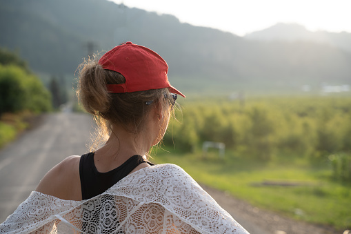 Woman wearing a red ballcap and a white lace shawl looks out on the rural landscape during the golden hour. Concept for dreaming, thinking, admiring