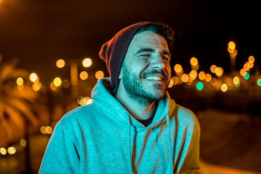 Man laughing and wearing casual clothes and a wool hat at night