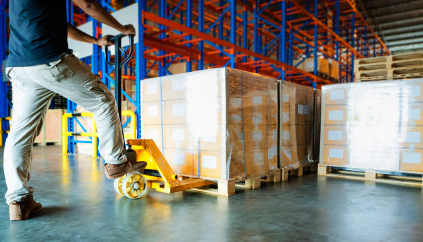 istock warehouse worker working with hand pallet truck and cargo shipment pallet at distribution warehouse, stacked of package boxes on wooden pallet cargo export for transportation. 1168229648