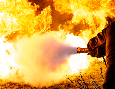 A man pointing a burst of carbon dioxide from a fire extinguisher towards the base of a fireball.