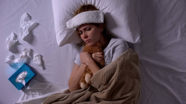 istock Lonely sick woman hugging teddy-bear lying in bed with compress and tissues 1168236553