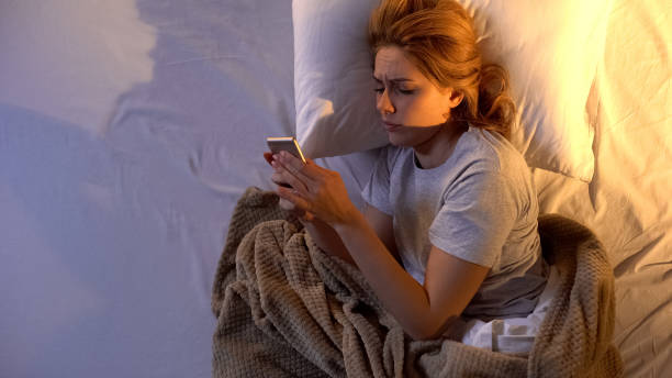 Sleepy girl turning off alarm clock and checking to-do list for today on phone Sleepy girl turning off alarm clock and checking to-do list for today on phone cross off stock pictures, royalty-free photos & images