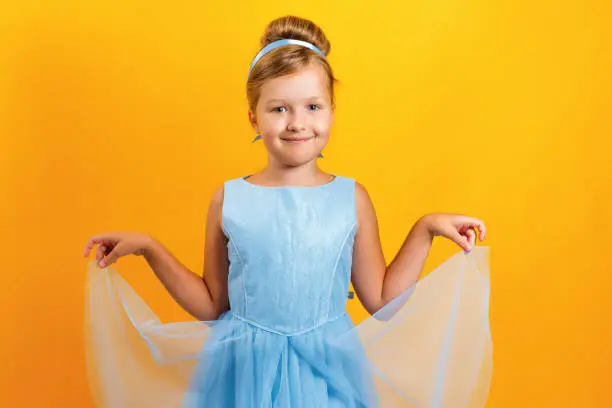 Photo of Charming little girl in a costume of Princess Cinderella on a yellow colored background. Concept for autumn, holiday, halloween.