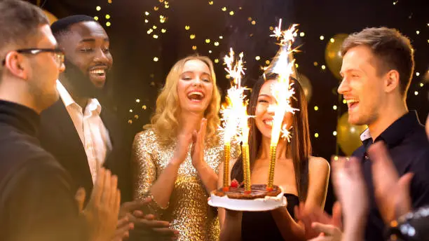 Photo of Pretty woman in party hat carrying cake with fire candles, celebrating birthday