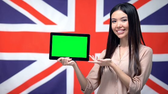 Girl holding tablet with green screen, British flag on background, migration