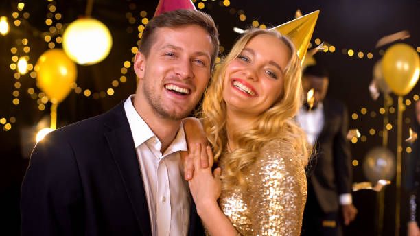 istock Excited couple smiling on camera standing under falling confetti at night club 1168237945