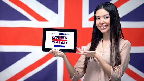 Lady holding tablet with learn English app, Great Britain flag on background
