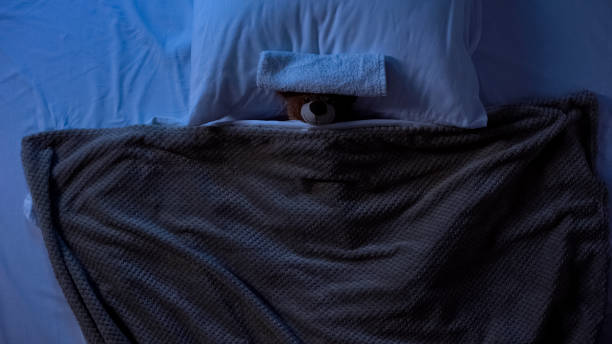 istock Toy teddy bear lying in bed under blanket with towel on forehead, fever weakness 1168238010