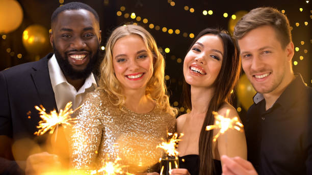 istock Four multi-racial friends smiling on camera holding bengal lights and glasses 1168238044