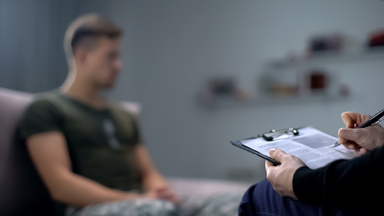 Psicólogo tomando notas durante la sesión de terapia con el soldado masculino triste, PTSD photo